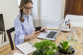 女人在家里的木桌上使用手机和笔记本电脑