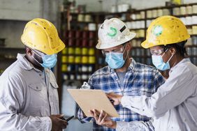 一名妇女和两名男子戴着口罩在工厂工作。