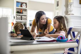 一个女人趴在桌子上，指导两个孩子中的一个做作业。