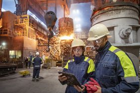 在炼钢厂，男女炼钢工人在倒钢时使用数字平板电脑