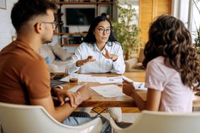 A man and a woman talk to a banker as papers are spread on a table between them.