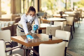 带着口罩和手套的女服务员在咖啡馆用消毒剂清洁桌子