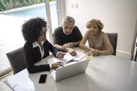 Businesswoman and older couple consult laptop and paperwork at home