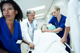 医生和护士推着病人通过ER在担架上,手里拿着氧气罩在自己脸上”>
          </noscript>
         </div>
        </div>
       </div>
       <div class=