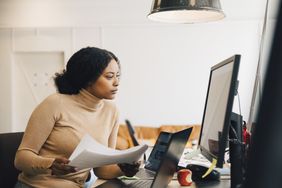 专注的女性IT专业人士拿着文件，看着电脑在创意办公室