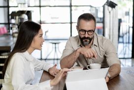 一个女人和一个男人坐在咖啡店看平板电脑”width=