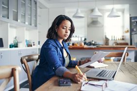 一个女人坐在桌子面前的笔记本电脑拿着文档和用铅笔写