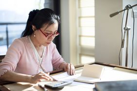 A worried woman uses a calculator to add up her credit card debt