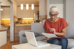 一个女人坐在笔记本电脑前在她的家里,看起来在文书工作。