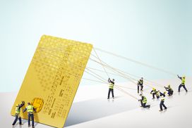 一群建筑商举起了一张巨大的信用卡，象征着一张有担保的信用卡将如何重建不良信用＂width=