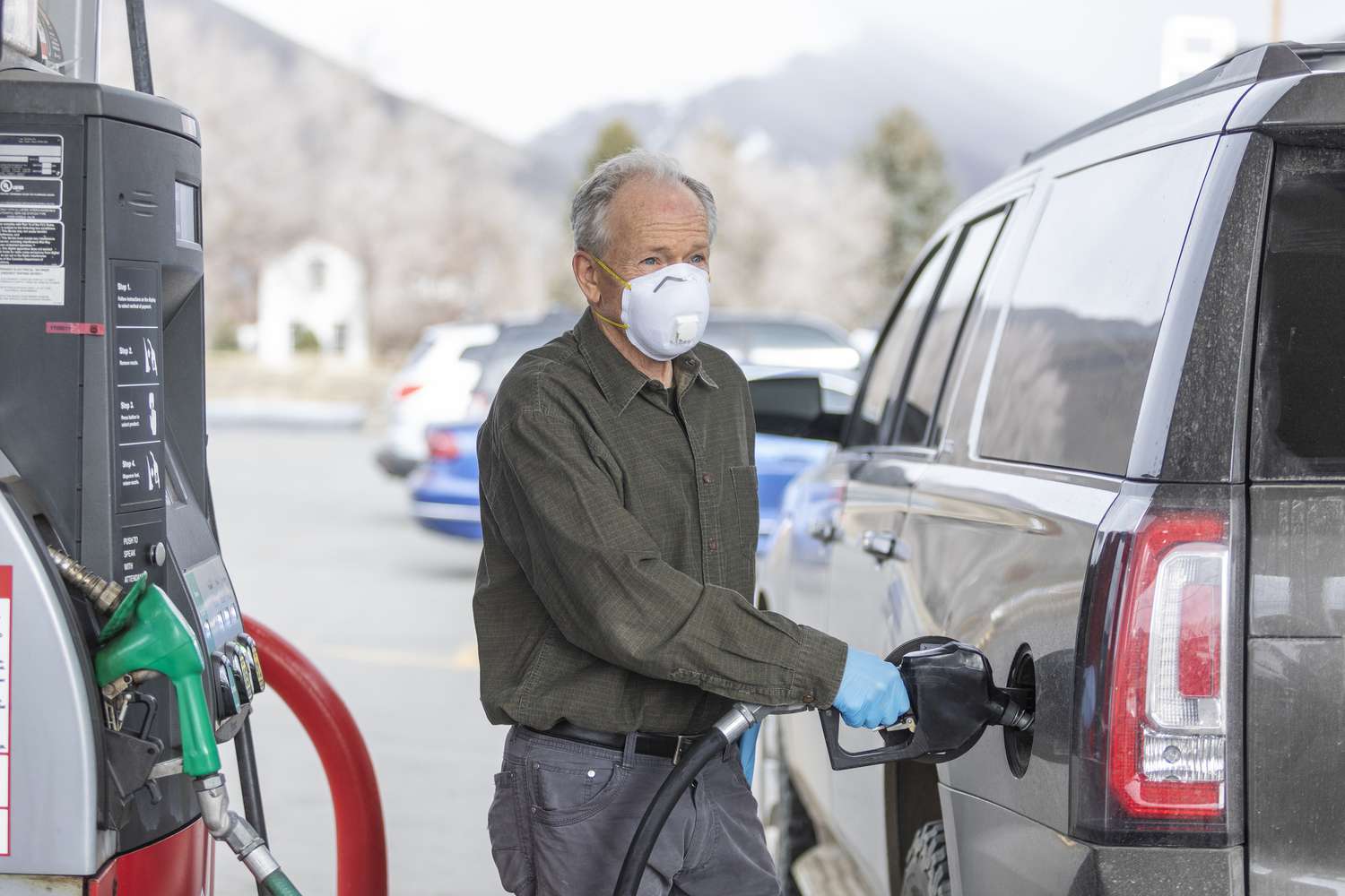 男人戴外科手套和口罩在加油站加油的车。”class=