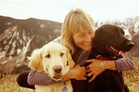 一个成熟的女人抱着她的两条狗在山上