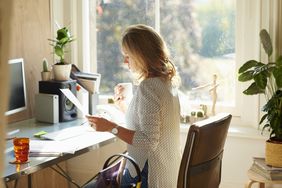 女人在阳光明媚的家庭办公室喝咖啡和阅读文件