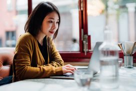 美丽的年轻女子使用笔记本电脑坐在咖啡馆＂width=