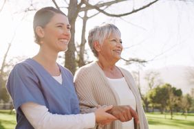 Nurse and older woman walk arm-in-arm in the sun