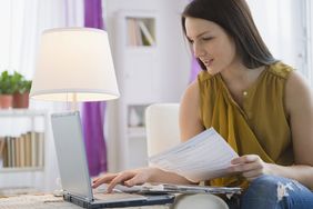 一个女人坐在沙发上用笔记本电脑工作，手里拿着文件