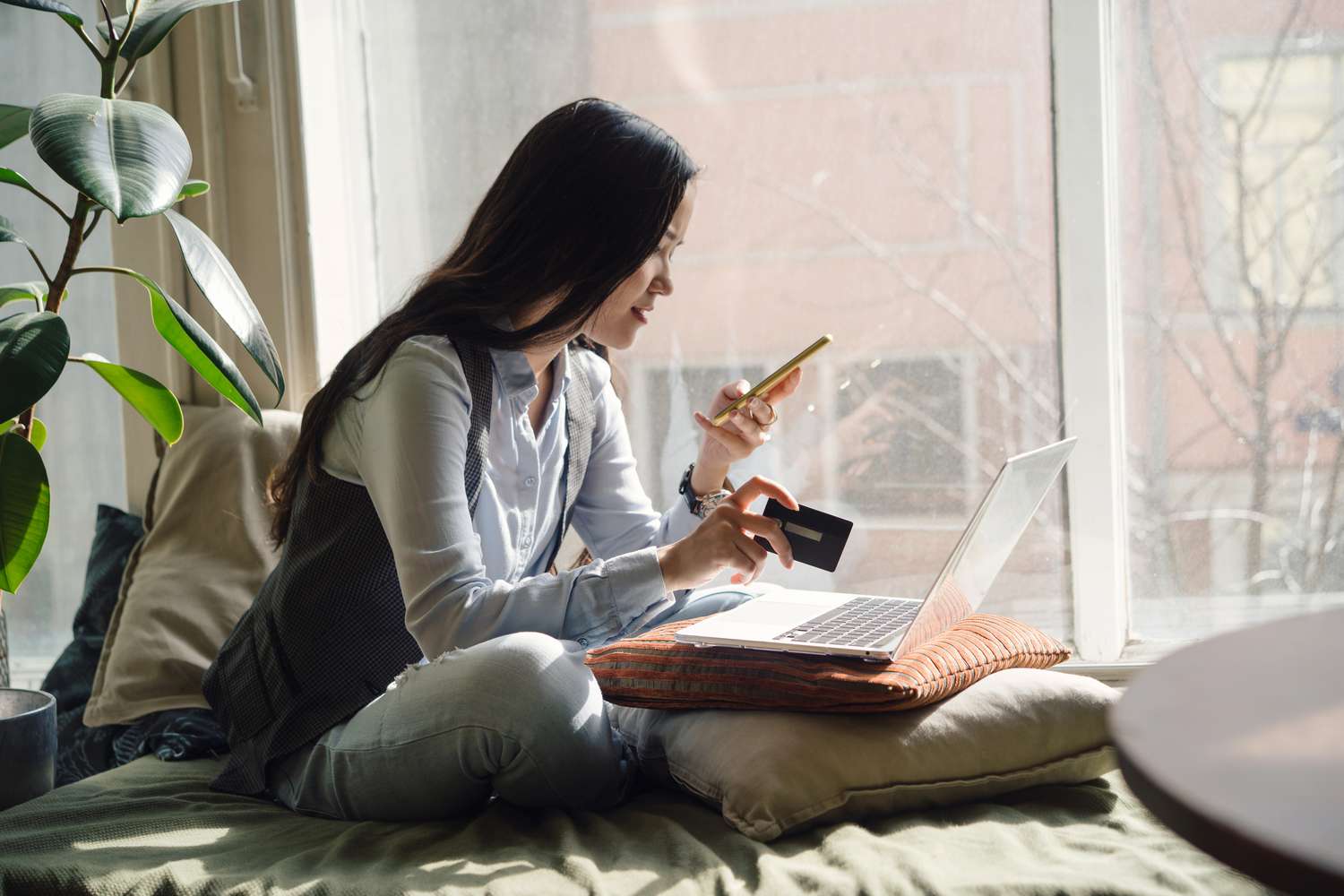 亚洲一个中年女人在蓝色牛仔裤坐在床上瑜伽姿势的笔记本电脑——库存图片