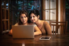 妈妈和女儿坐在一张木桌前看电脑