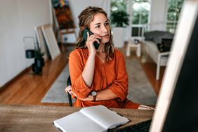 Woman business owner speaks on phone with private lender while sitting at a desk with a notebook