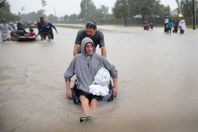 一名男子推着另一名坐在轮椅上的男子穿过哈维飓风带来的洪水