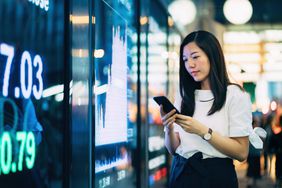 自信的年轻亚洲女商人检查智能手机上的金融交易数据。