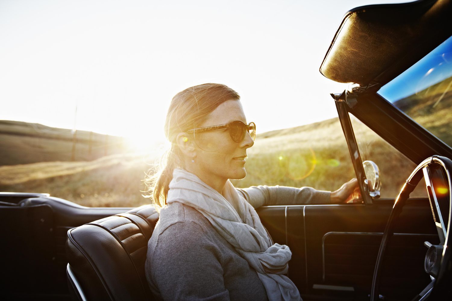 成熟的女人戴着太阳镜在日落时开车＂class=