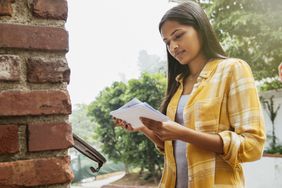 Young woman looks through her mail at a mailbox