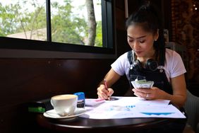 一位女企业家一边喝着咖啡，一边拿着纸和笔在桌子上数钱