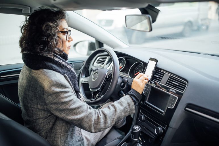 一位女士坐在她的车里，看着她的手机，手机安装在通风口上，通过远程信息技术跟踪她的驾驶情况