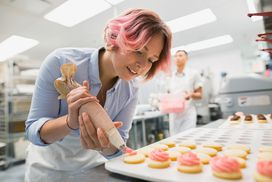 Pastry chef piping cookies pink icing commercial kitchen