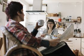 一对夫妇在厨房讨论财务问题。一个拿着报纸和杯子。