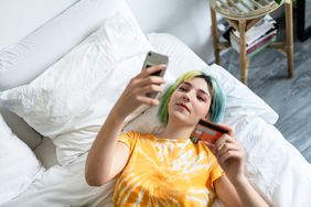 一个女人在床上和她的手机和信用卡网上商店。