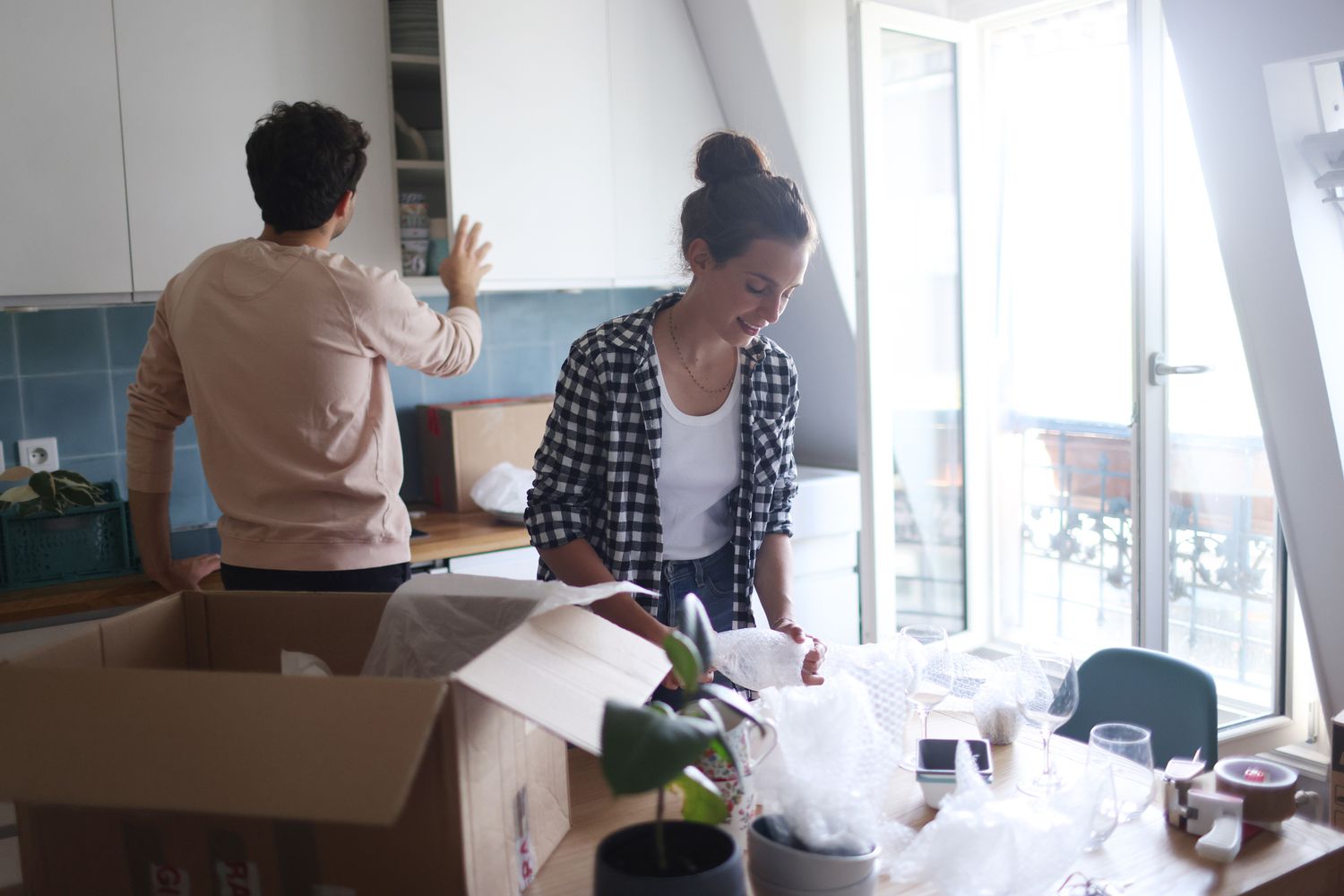 一对年轻夫妇在一个干净明亮的地方打开装有厨房工具和用品的移动盒子。＂class=