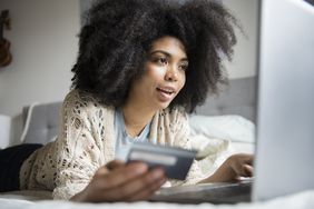 非裔美国妇女躺在床上用笔记本电脑网购。