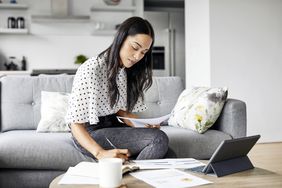 A woman sits on a couch with a tablet and pen calculating loan principal