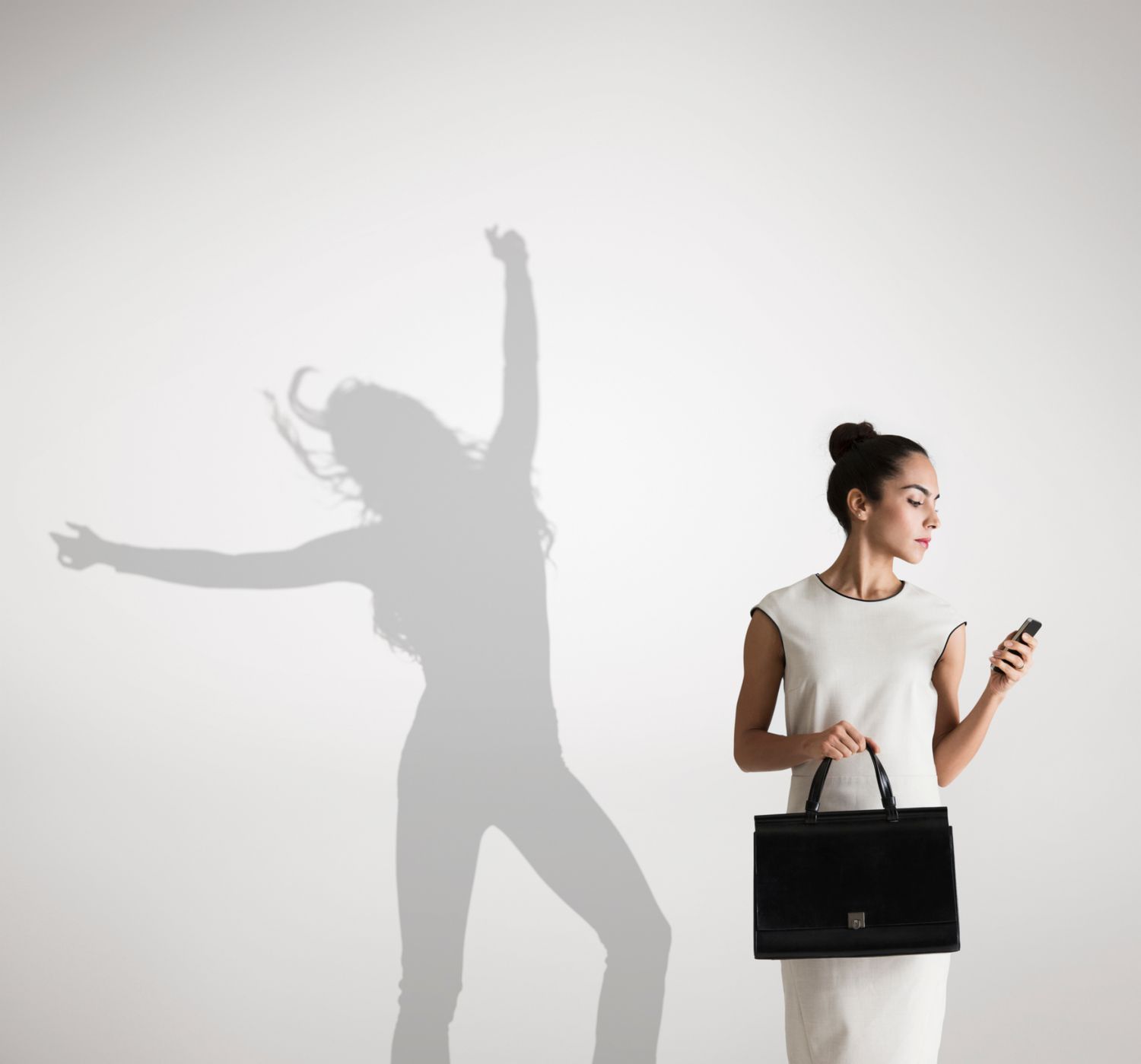 一个女商人看着自己的工作手机在自己的影子前跳舞，代表着工作与生活的平衡。