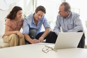 一男一女和另一男坐在一起，他们拿着笔记本电脑和眼镜在桌子上签署一份文件