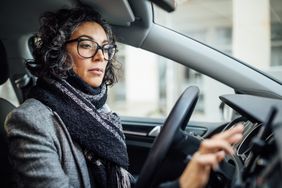 目不转睛地盯着一个女人开车一辆车看起来在一个智能手机安装在仪表板和水龙头在屏幕上用她的食指。