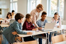 老师和年轻学生在教室里使用笔记本电脑。