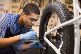 穿着蓝色条纹衬衫的年轻人在自行车修理店修理自行车齿轮。
