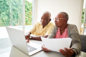 一对老年夫妇在家里的桌子上用笔记本电脑处理他们的税务