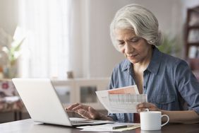 一名年长的妇女一边拿着文件，一边在笔记本电脑上工作