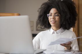一个女人和一篇论文在她的手,看着她的电脑屏幕