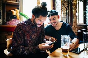 两个男人在一家精酿啤酒酒吧边喝酒边看智能手机
