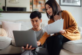 一个男人和一个女人在沙发上看文件和笔记本电脑。
