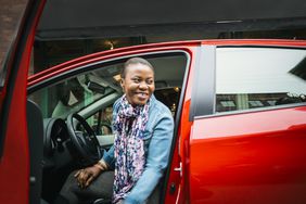 一辆红色汽车的司机从敞开的车门里微笑着。