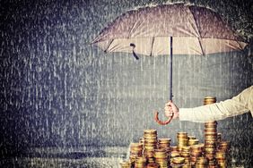 一名男子在一堆硬币上撑着伞，以保护资产不受雨淋