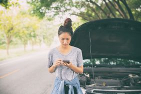 Young woman on cellphone near car with open hood