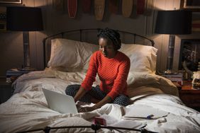 年轻女子坐在床上使用笔记本电脑在晚上