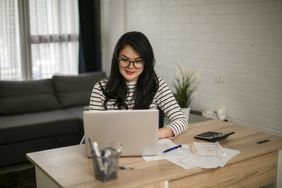 Woman at wooden desk works on laptop at home